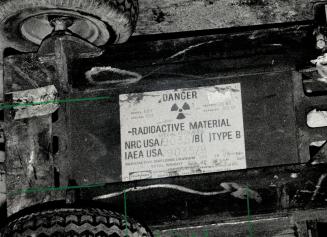 Constable David Fitzgerald (left) and Bill May of the Atomic Energy Control Board check container for radiation after it fell off a truck. Label (inset) warns of radiation hazard. Story A3