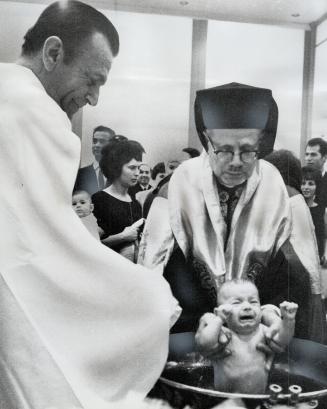 Baptism Greek Style, Archbishop Theodosios, head of the Greek Orthodox Church in Canada, baptizes one of twin children of Mr. and Mrs. Nickos Kotas at(...)