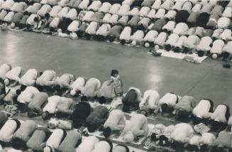 Overhead view of large number of people bent over praying with a young girl standing and a path ...