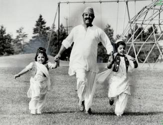 A man in traditional Muslim attire is flanked by his two children, also in traditional attire.