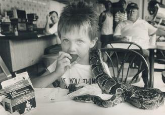 Trik's treat. Trik Stockley, 4, enjoys a cookie at a downtown doughnut shop yesterday while his pet python, killer, hangs around looking for crumbs. T(...)