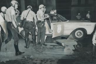 Shotgun blast victim Patrolman Joseph Hennigan lies by a squad car as racial rioting flared for the second straight night in Buffalo's Negro ghetto last night
