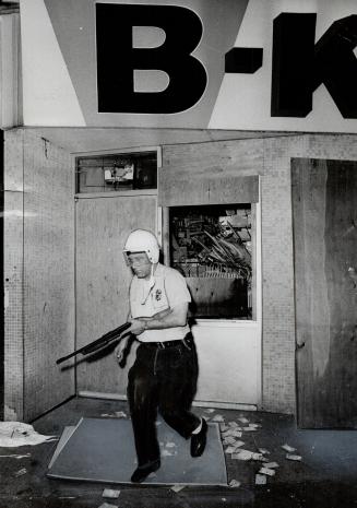 Armed and helmeted, a Buffalo patrolman cautiously passes the B-Kwik Food Market where Negro youth were reported looting last night