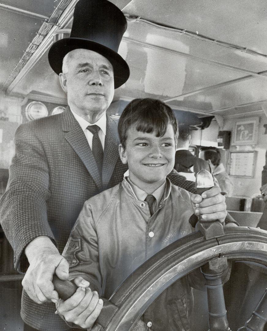 First ship enters port. Bruce Grout, 10, plays helsman at the wheel of oil carrier Imperial Windsor, while ship's captain James Irwin stands behind hi(...)