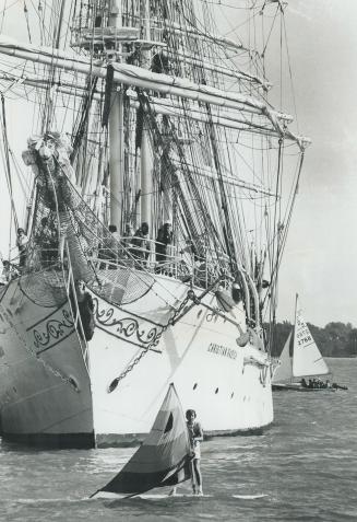 The Norwegian Windjammer Christian Radich towers over Arthur Langley, 25, as he sails tiny windsurfer in Toronto Harbor