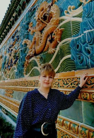A blonde woman leans against a colourful ceramic mosaic depicting a dragon and water.