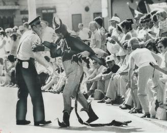 A Devil tempts a Metro policeman into a dance yesterday as the big Shriners parade rolled north, with its 135 bands so closely spaced that spectators (...)