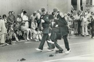 Two Keystone Kops with a prisoner execute some fancy footwork as they clown up University Ave