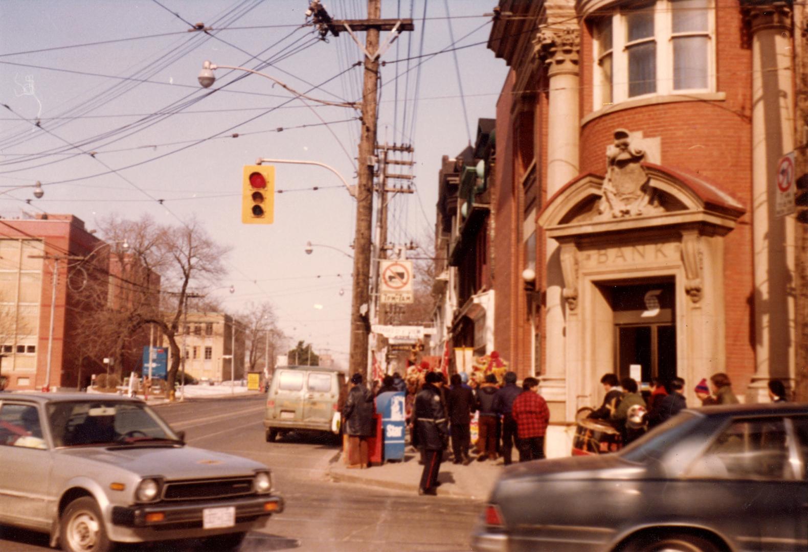 Shows a bank on the northeast corner of Broadview and Gerrard. People wearing warm clothes are  ...