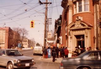 Shows a bank on the northeast corner of Broadview and Gerrard. People wearing warm clothes are  ...