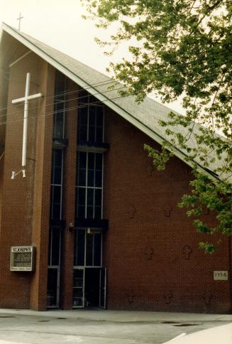 Image shows a part of the church building front side with a church sign and a big cross closer  ...