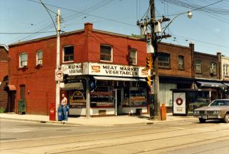 Image shows a few two storey buildings at the intersection. There is a sign on the corner build…