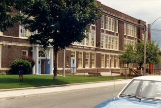 Image shows a three storey school building from the street side with some trees in front of it.