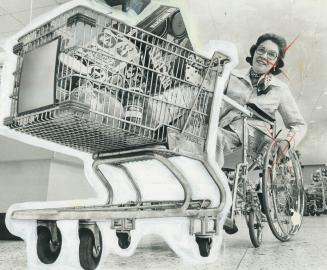 First Handicapped person to try out attachment for shopping carts, Elizabeth Condon McKenzie guides it around a supermarket yesterday. I think it's a (...)