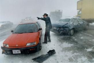 Storm tossed: Peel Constable Evan Smith, top, directs a damaged car yesterday amid high winds that also tore at Toronto pedestrians