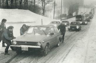 A group of boys have fun pushing cars up an incline on York Mills Rd