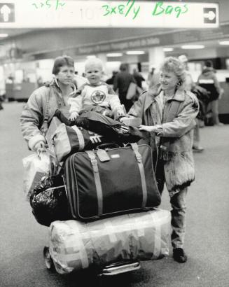 Weary Hazel Rolfe (left) pushes cart loaded with luggage and her nephew, Jason, while the tot's mother, Anne Rolfe helps guide it. They were on their way fromTerminal 2 to Terminal 1