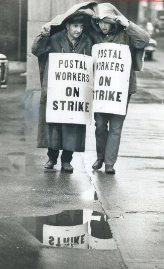 Sharing shelter from the rain, striking postal workers Bob Johnson (left) and Art Langley picket the main postal building today while officials were b(...)