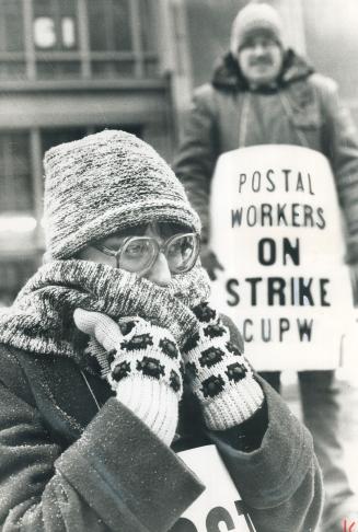 Bundled against cold, striking postal clerk Ilona Laney huddles today in the picket line on Front St