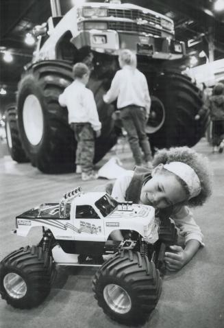 Miniature monster, Andrea Halford, 6, plays with a radio-controlled model of a USA-1 monster truck as the real thing looms in the background at The Hobby Show yesterday