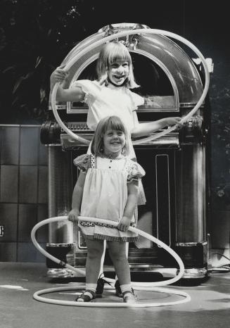 Hula hoop rock, Suzanne Punfield, 9, and baby sister Jaime, 3, do a hula hoop hop to a juke box rock as fifties fever swept through Don Mills Centre