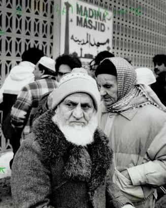 Man with full white beard wearing tuque looks left, unsmiling. 