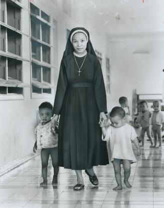 Sister Theresa Khen, one of nine nuns who care for 1,245 young orphans, walks with two little ones