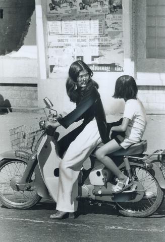 Traditional and mod blend on young lady on motorcycle, Square-heeled shoes and sunglasses are now popular in Saigon