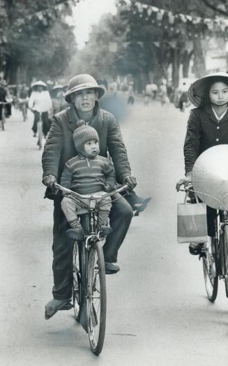 A small boy, well bundled-up, gets a lift on a bicycle, the principal means of transport in Hanoi, unlike Saigon with its motor scooters
