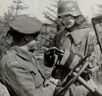 Completely Clad in Germany garb, even to the helmet, this Polish woman on guard at Haren camp is here inspecting the identity card of Driver William M(...)