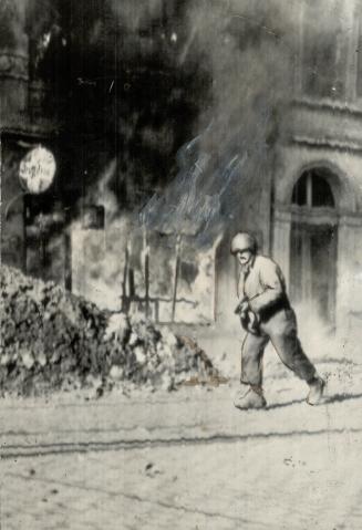 A Yank infantryman slogs past a burning building in Aachen as he advances into the city