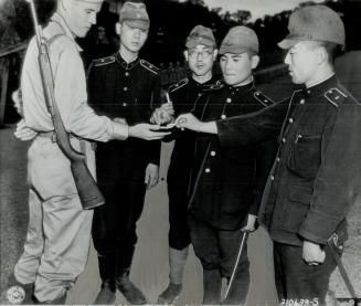An unidentified allied soldier is shown here sharing his cigarettes with four members of the imperial palace guard at Tokyo
