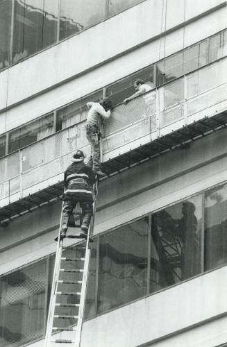 Fireman Duke Mitchell helps window-washers Ron Lyons and Bruce Cormier, both 25, climb to an aerial ladder after they were trapped today on their plat(...)
