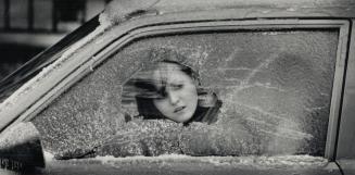 Thick ice: Lena Bouffard peers out through her car's window while waiting for her boyfriend to finish chipping away the ice