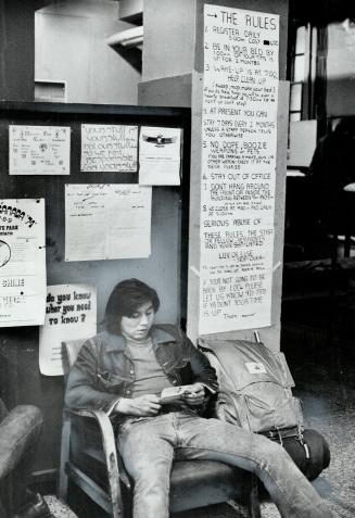 Young Traveller rests at Stop-Over, behind him the list of rules posted in hostel's lobby