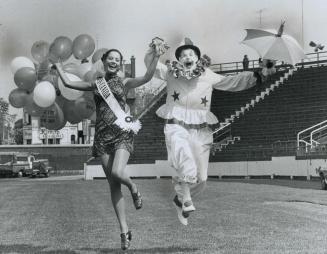 In high spirits, Miss Canada (Carol Commisso) and Yum-Yum the clown fly through the air just before the start of the Red Cross society parade from Var(...)