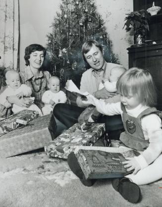 Big sister Katie, 2, gives her baby sisters a demonstration of how to get a Christmas present out from under that wrapping while parents, Gretchen and(...)