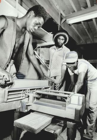 Wayne Wells (centre), the guiding force behind Immi-Can, watches while workers Kamau (left) and Henry Davison operate wood-working machinery at plant (...)
