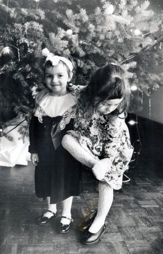 Jacquie Moir, 3, left, smiles as Timea Keller, 4, leans on her while checking her stockings yesterday