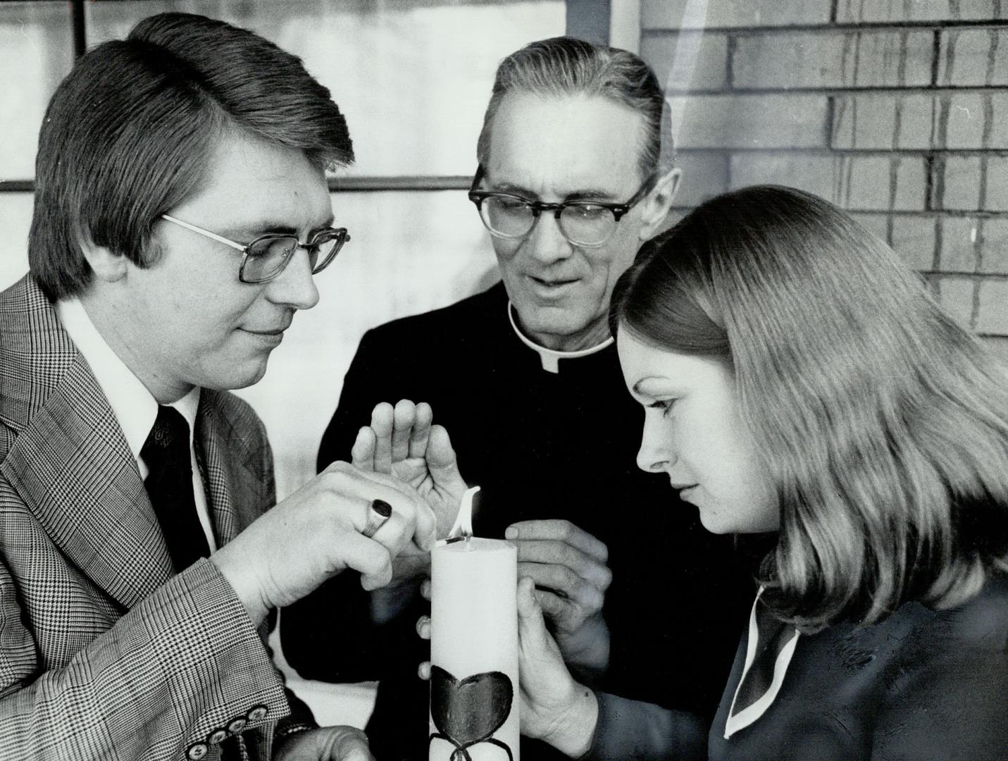 John and Mary Huff are seen with Father Patrick German and are lighting a candle, a symbol of marriage encounter program priest conducts. The Huffs, w(...)