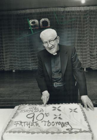 Reverend Thomas Toomey cuts a giant 90th-birthday cake presented by parishioners at party