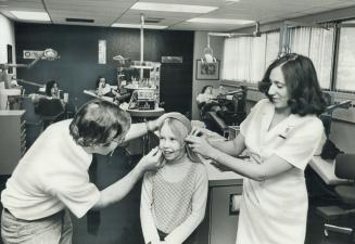 Lynne Kiddey, 10, doesn't seem to all unhappy about having a teeth straightener fitted by Dr. Ron Teitler and Diane Bagnell, a registered nurse. Altho(...)