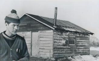 A Saskatchewan Metis stands beside his one-room log cabin