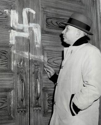 Swastika on Synagogue on St. Andrew's St., just a few doors from busy Spadina Ave., is examined by Sol Feldman, a mourner. Police are putting an aroun(...)