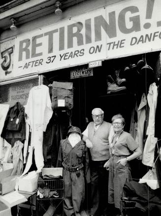 Man and woman stand in shop entrance surrounded by assortment of utility clothing and supplies  ...