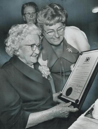She's 100 tomorrow, Mrs. Margaret Willoughby (left), who will be 100 tomorrow, reads a framed congratulatory scroll from Premier William Davis to her (...)