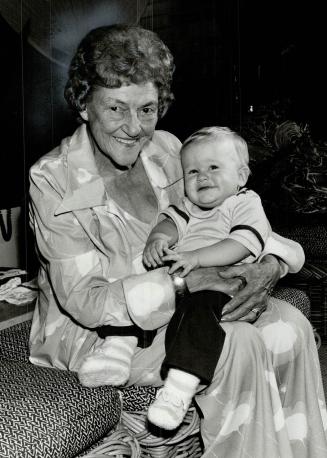 Image shows an elderly lady holding her great-great-grandson.