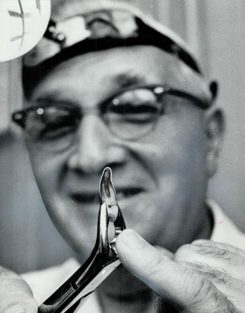 Holding extracted tooth in his forceps, Dr. Samuel Leslie