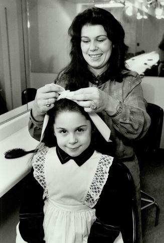 Finishing touch to her Elen Henderson ribbon-and-lace outfit is applied to model Vivi, 6, by her mother, Vida Farella, before pictures are taken