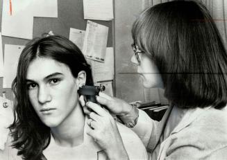 Sugrical gun is used by Paige Richmond to put a steel stud into the ear lobe of David Gregory, 15